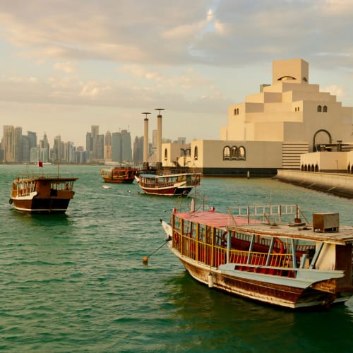 Boats floating in Doha's waterfront with city skyline and modern architecture in the background.