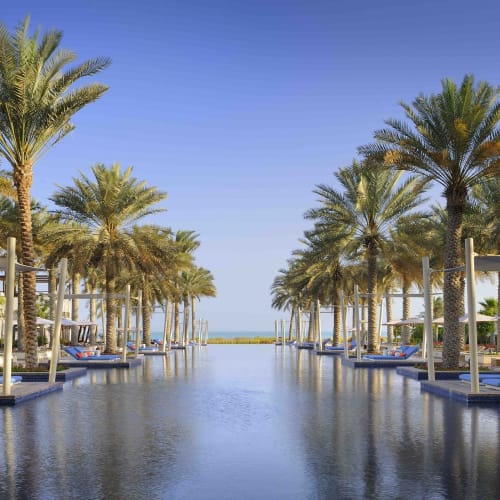 Luxuriöser Infinity-Pool mit Palmen und Liegestühlen am Wasser, in einer tropischen Resort-Umgebung.