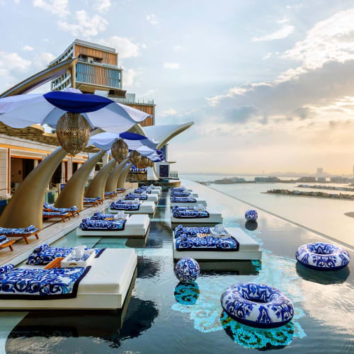 Luxuriöser Poolbereich bei Atlantis The Royal mit Liegestühlen, Sonnenschirmen und Wasserbällen, Blick auf die Stadtskyline bei Sonnenuntergang.