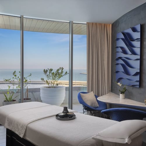  Spa-Zimmer mit Massageliege, großen Fenstern mit Meerblick und moderner Dekoration.