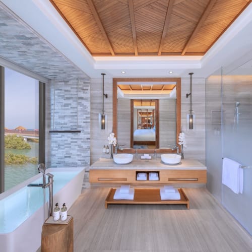 Luxuriöses Badezimmer mit Doppelwaschbecken, großem Fenster mit Blick auf Wasserweg und eleganter Dekoration mit Blumen und Holzakzenten.