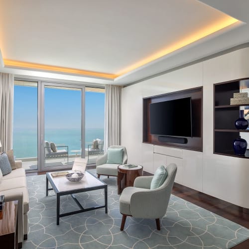 Elegantes Wohnzimmer mit Meerblick, mit Sofa, Sesseln, Couchtisch, großem Fernseher und Balkon mit Sitzgelegenheiten.