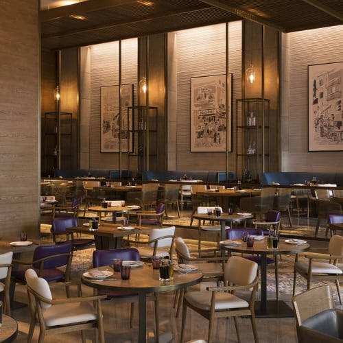 Empty restaurant with several tables, chairs, and soft lighting on the walls, decorated with artworks.