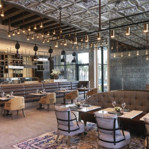 A stylish restaurant interior with plush seating, modern lighting, and a bar area in the background.
