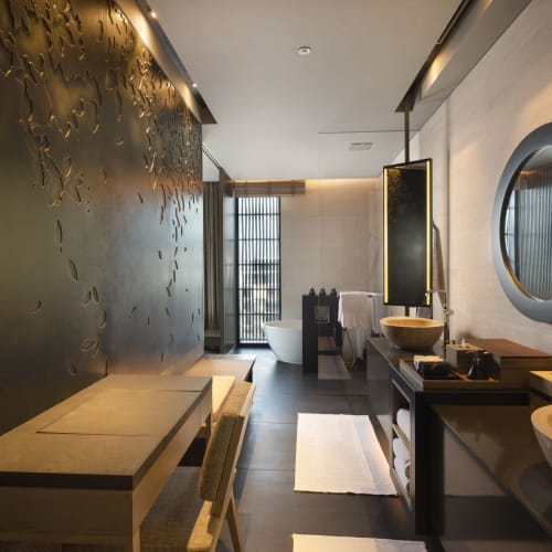 Luxurious hotel bathroom with modern decor, featuring two vessel sinks, a round mirror, and a bathtub in the background.