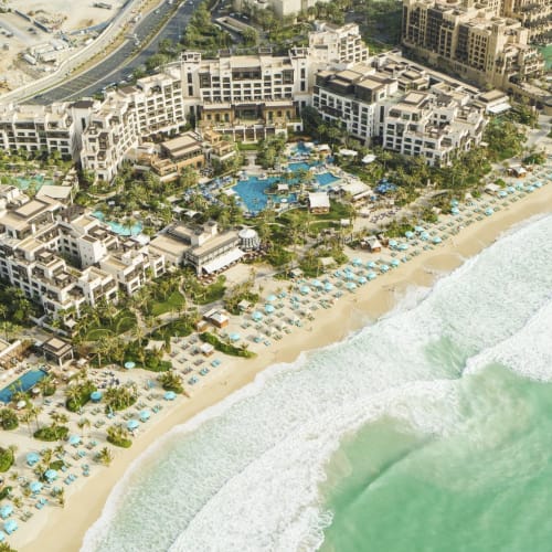 Aerial view of a beachfront resort with numerous swimming pools, beach umbrellas, and modern buildings near the ocean.