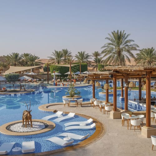 Ein luxuriöses Wüstenresort mit großem Pool, umgeben von Palmen, Liegestühlen und schattigen Sitzbereichen.
