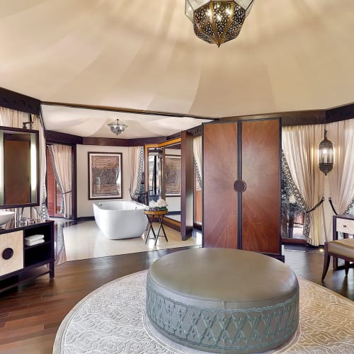 Luxurious bathroom in a tent-like setting with wooden partitions, large windows with curtains, and elegant decor.
