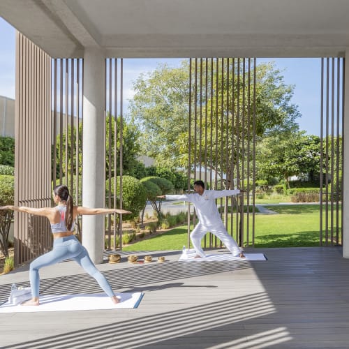 Two people practicing yoga outdoors on a wooden deck with a garden background.