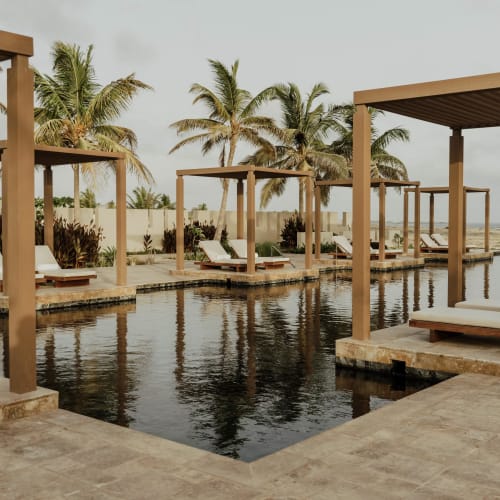 Luxus-Poolside-Cabinas mit Liegestühlen in einem tropischen Resort, mit Palmen im Hintergrund.