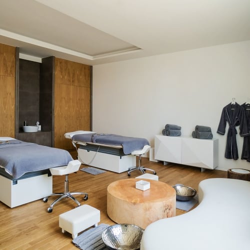 A well-appointed spa room with two massage beds, a seating area, and bathrobes hanging on the wall.