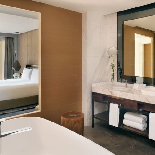 Modernes Hotelzimmer mit Blick auf die grüne Außenanlage, mit Badezimmer mit Marmorspüle und Spiegel sowie Badewanne.
