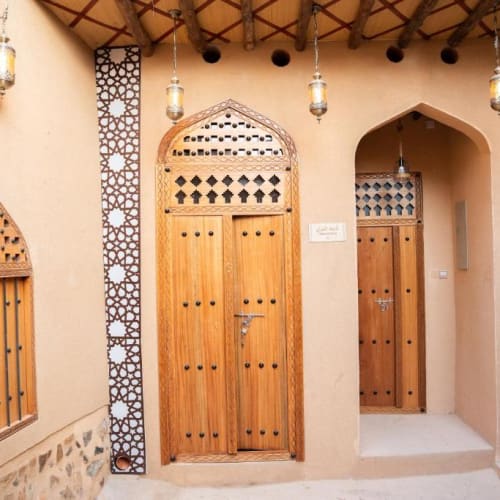 Drei Holztüren mit kunstvollen traditionellen Schnitzereien in einer hellbeigen verputzten Wand unter hängenden Laternen in einem Gebäude im Nahost-Stil.