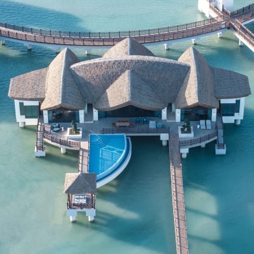 Luftaufnahme eines luxuriösen Resorts mit traditioneller Architektur, umgeben von klarem Wasser und verbundenen Gehwegen.