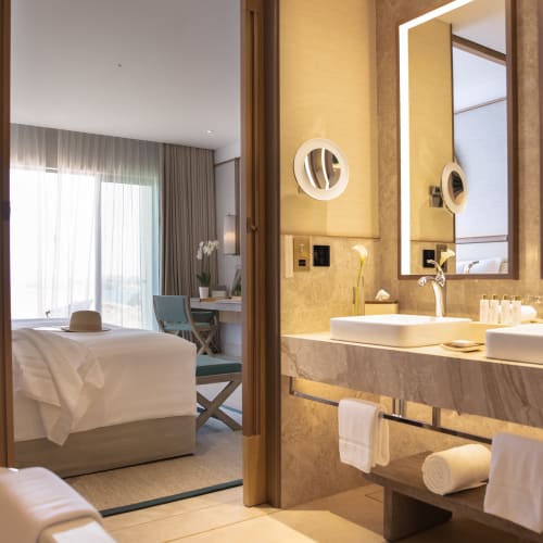 Ein luxuriöses Hotelzimmer mit Blick ins Badezimmer, das zwei Waschbecken, Spiegel und modernes Dekor zeigt.