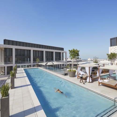Dachpool mit Leuten, die sich an Sonnenschirmen auf einem sonnigen Tag in Doha entspannen.