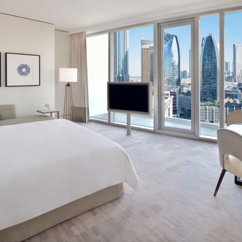 Modernes Hotelzimmer mit großem Fensterblick auf eine städtische Skyline, einschließlich Wolkenkratzer und ikonischer Gebäude.