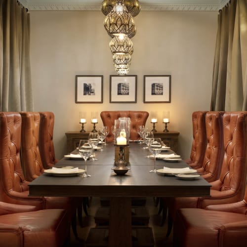 Eleganter Speiseraum mit einem langen Holztisch, umgeben von hohen Ledersesseln, dekoriert mit Kerzen und eingerahmten Bildern an der Wand.