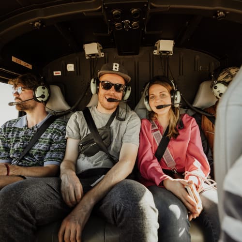 Drei Personen sitzen in einem Hubschrauber, tragen Kopfhörer und genießen den Flug.