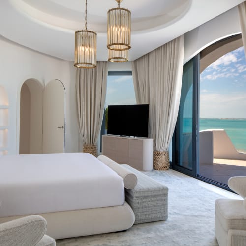 Luxuriöses Schlafzimmer mit Balkon mit Blick auf das Meer, mit weißen Möbeln und eleganten Vorhängen.