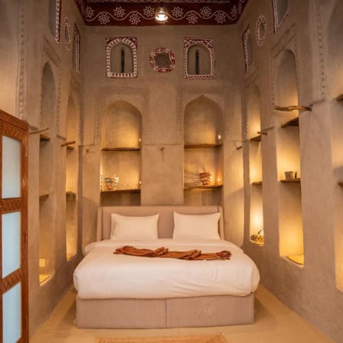 Gemütliches Schlafzimmer im traditionellen nahöstlichen Stil mit Doppelbett, eingelassenen Regalen in beigen strukturierten Wänden und warmem, weichem Licht.