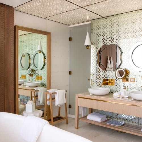 Luxurious bathroom with twin sinks, round mirrors, and a bathtub, featuring elegant decor and natural light.