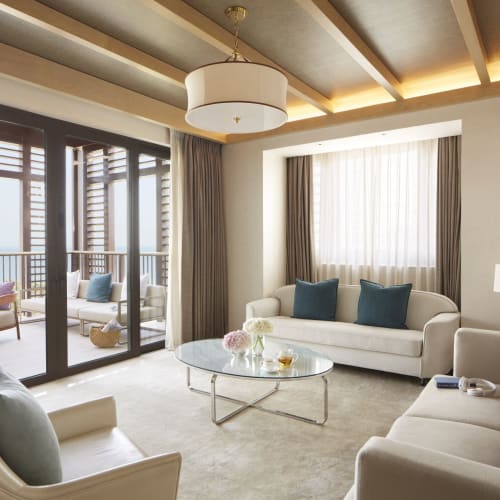 Luxuriöses Hotelzimmer mit weißen Sofas, einem Glastisch und großen Fenstern mit Balkonblick und buitenmöbel.