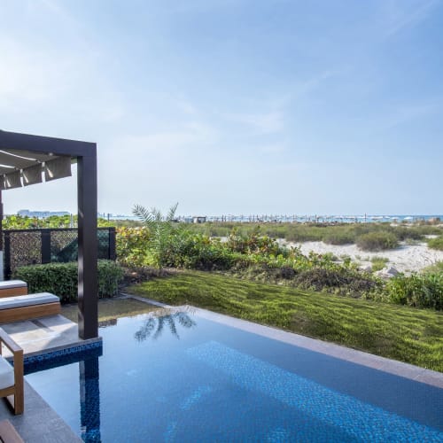 Ein luxuriöser Außenpoolbereich mit Liegestühlen und Blick auf einen sandigen Strand und das Meer im Hintergrund.