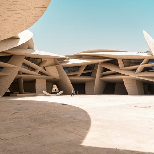 Modernes architektonisches Design des Doha National Museum mit komplexen, organischen Formen und offenem Raum unter klarem Himmel.