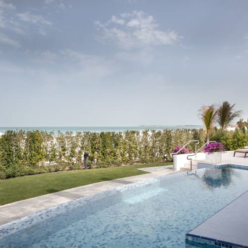 Luxus-Hotelpoolbereich mit Blick auf den Strand und das Meer, mit Liegen und Sonnenschirmen.