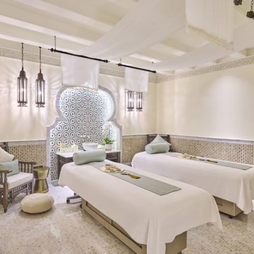 Two massage beds in a luxurious spa room with white curtains and Moroccan-style lanterns.
