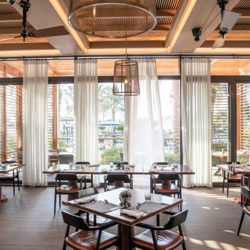 Elegantes Restaurantinterieur mit großen Fenstern, weißen Vorhängen und modernen Hängeleuchten