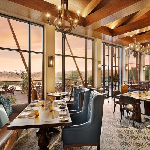 Elegant restaurant interior with large windows, wooden ceiling, and a mix of modern and vintage furniture.