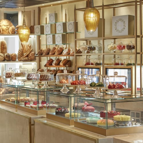 Eine elegante Bäckerei, die eine Vielzahl von Kuchen, Gebäck und Backwaren in Glaskästen in einem gut beleuchteten Geschäft präsentiert.
