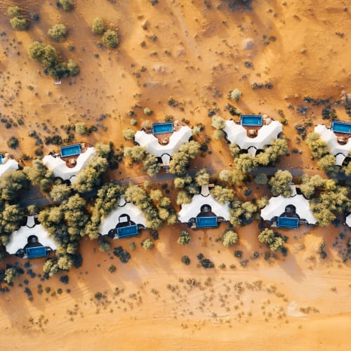 Luftaufnahme von Luxushütten in einer Wüstenlandschaft mit Palmen und Sandboden