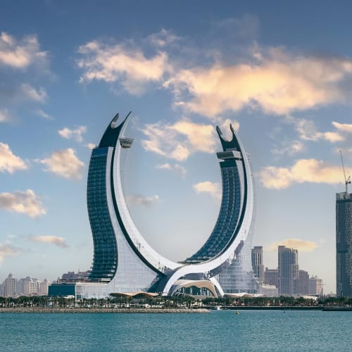 A modern architectural building shaped like a horseshoe with a city skyline in the background.