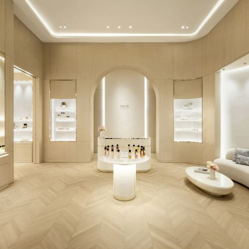 A luxurious, modern retail space with minimalist white decor, illuminated display shelves, and a beige herringbone wooden floor.