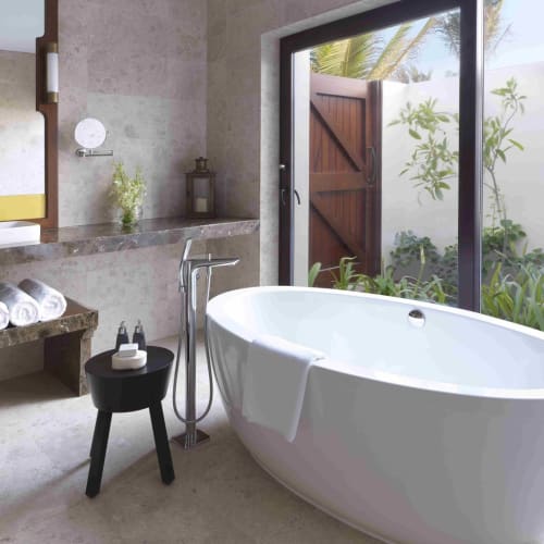 Luxurious bathroom with a freestanding bathtub overlooking a garden through large glass doors.