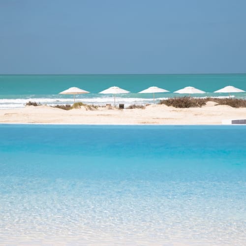 Eine ruhige Strandlandschaft mit klarem blauen Wasser, Sandstrand und mehreren weißen Sonnenschirmen.