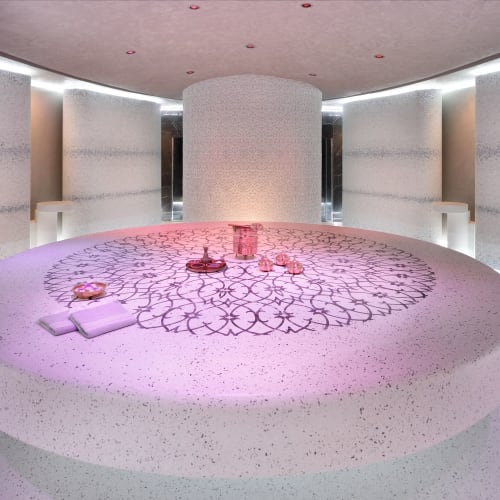 Ein minimalistischer, moderner Lounge- oder Veranstaltungsraum mit einem kreisförmigen, leuchtenden Tisch in der Mitte, umgeben von hellen Wänden und Bänken.