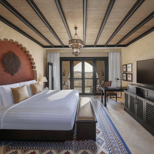 Luxurious hotel room with a large bed, a flat-screen TV, and a balcony overlooking desert scenery.