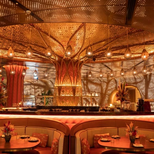 Luxuriöses Restaurant-Interieur mit aufwändiger Beleuchtung, bequemer Sitzmöbel und dekorativen Bäumen, die eine warme, elegante Atmosphäre schaffen.