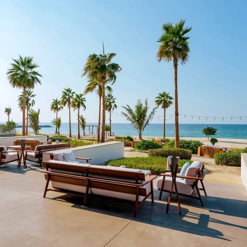 Outdoor seating area at Nikki Beach Resort & Spa Dubai facing the beach with palm trees and a clear blue sky.