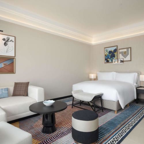 A luxurious hotel room with a bed, sofa, and modern art decor in a bright and spacious setting.