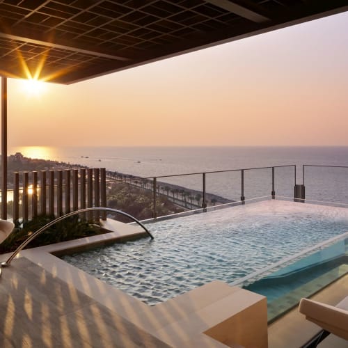 Sunset over a luxurious rooftop infinity pool overlooking the ocean with modern outdoor furniture.