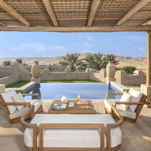 Eleganter Sitzbereich im Freien mit Blick auf einen Pool und Wüstenlandschaft im Hintergrund.