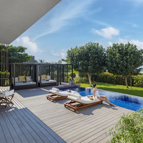Zwei Frauen entspannen auf Sonnenliegen in der Nähe eines Pools an einem Frontresort mit üppigem Grün und dem Meer im Hintergrund.
