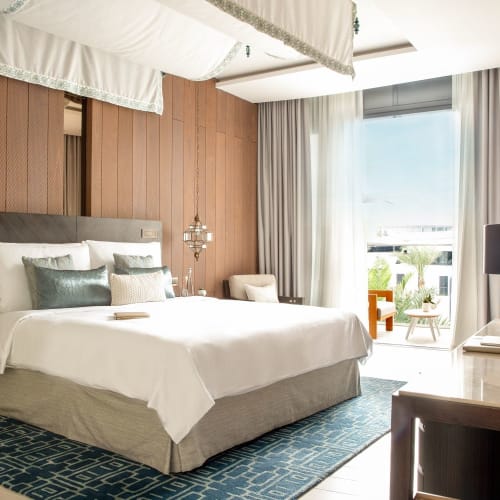 Luxurious hotel room with a large bed, wooden wall paneling, and a balcony overlooking the sea.