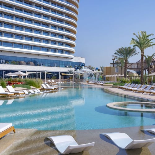 Luxus-Hotelpoolbereich mit Liegen, Palmen und einem modernen Gebäude im Hintergrund.
