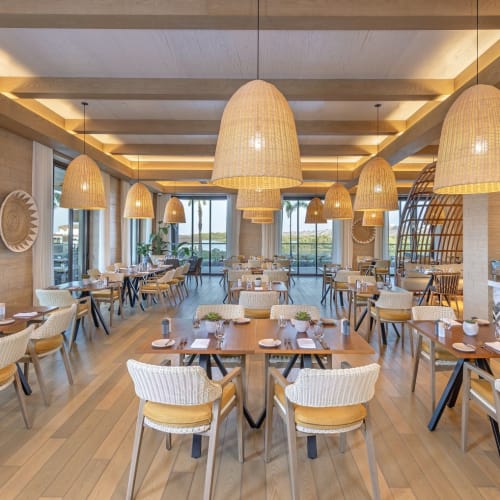 Eleganter Speisebereich in einem modernen Restaurant mit großen, geflochtenen Hängeleuchten, die von einer Holzdecke hängen.